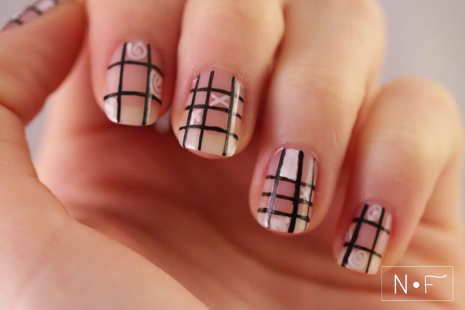 Curiosa manicura de uñas en beige, adornadas con líneas formando cuadros en color negro y blanco.
