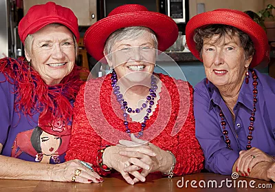 Tres mujeres mayores que desgastan los sombreros rojos.