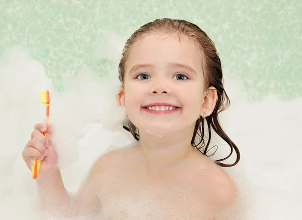 niña sonriente está tomando un baño con el cepillo de dientes ...