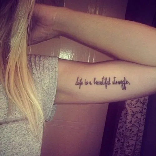 Pequeño tatuaje en el bícep que dice “La vida es una hermosa lucha ...