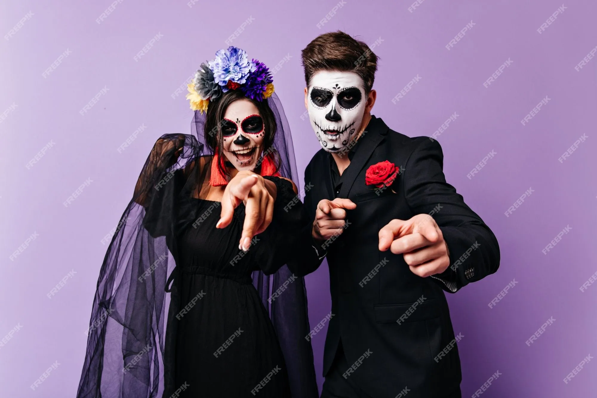 Chico alegre de pelo oscuro y su novia con caras pintadas para halloween  están sonriendo y mostrando los dedos a la cámara. | Foto Gratis