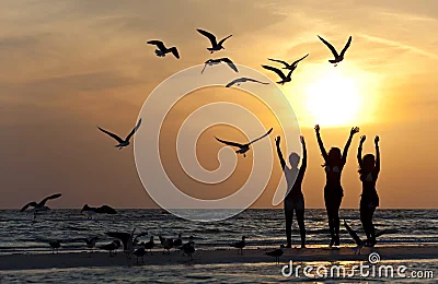 Tres mujeres jóvenes que bailan en la playa en la puesta del sol.