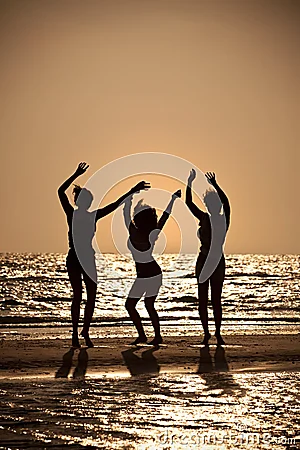 Tres mujeres jovenes que bailan en la playa en la puesta del sol.