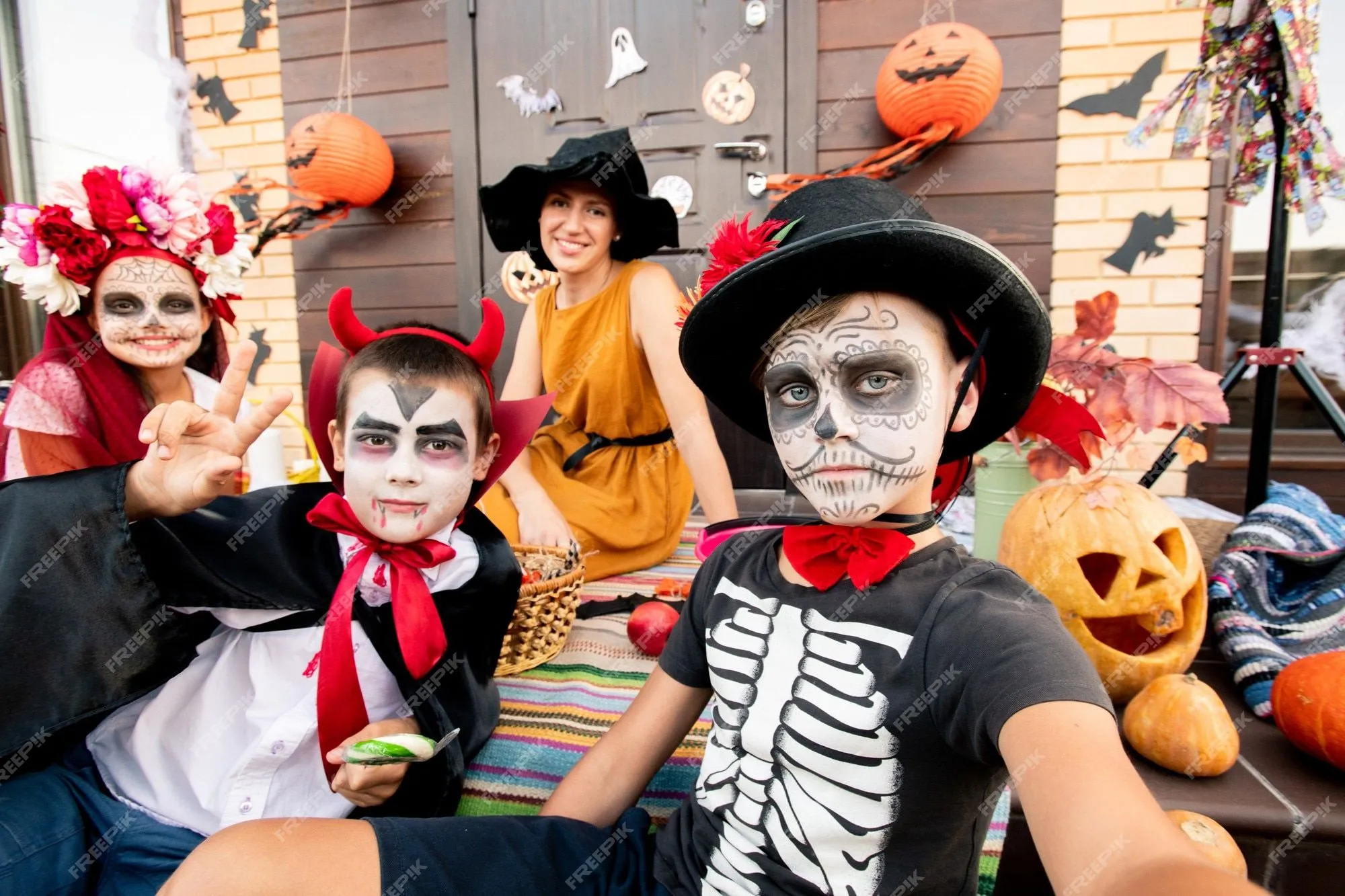Dos niños y una niña con las caras pintadas sentado en la escalera en el  fondo de la feliz joven elegante con sombrero de bruja negro y vestido  amarillo | Foto Premium