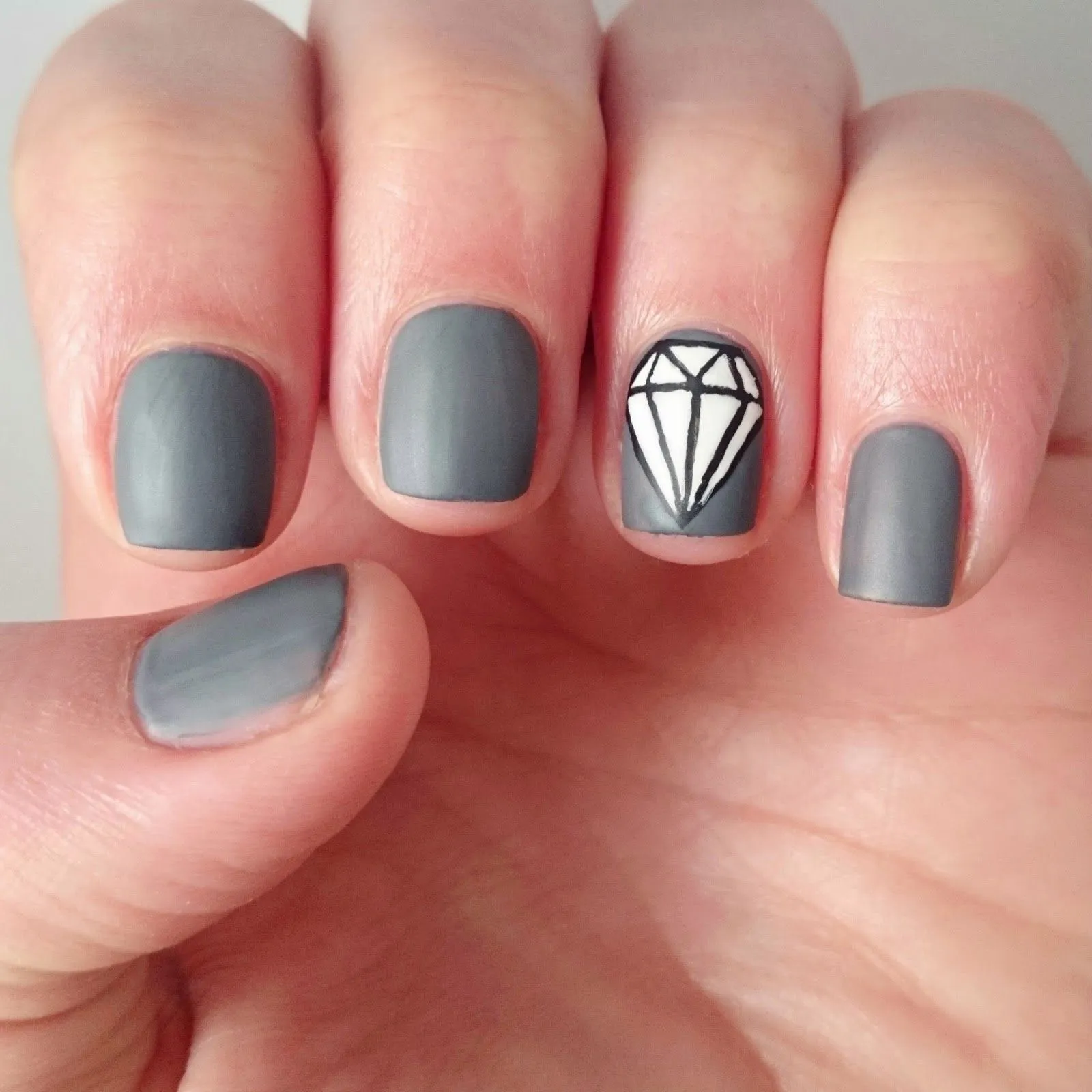 Uñas en gris mate, una de ellas decorada con el dibujo de un diamante en color blanco y negro.